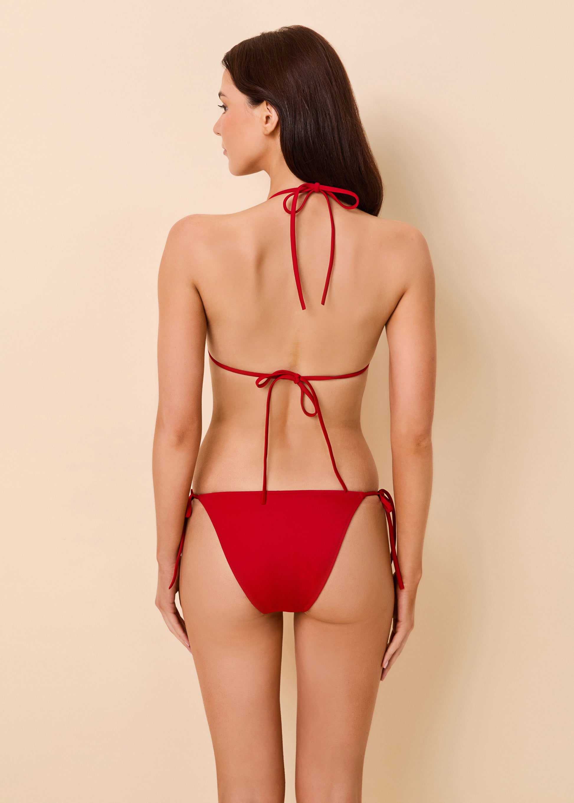 A woman shown from the back wearing a red string bikini against a plain beige studio background.