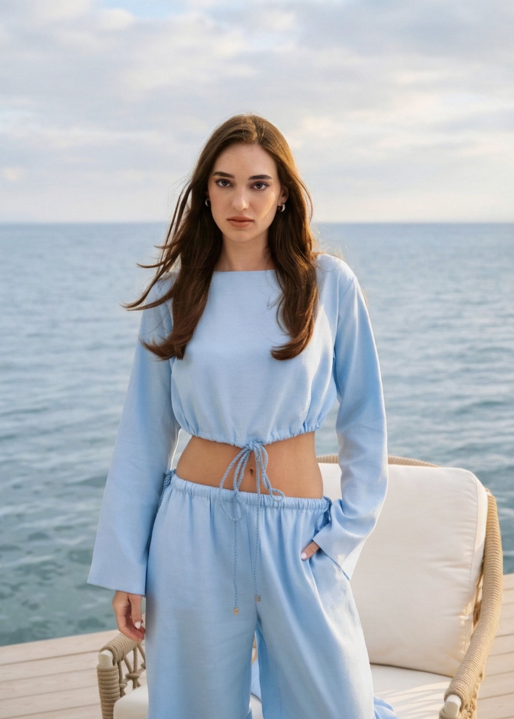 Woman in a light blue outfit standing on a boadockt with ocean and sky in the background