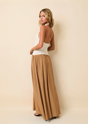 A woman modeling a sleeveless white halter-style top and a flowing tan maxi skirt against a plain beige studio background.