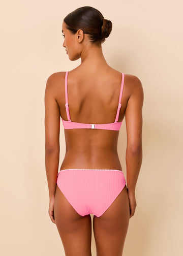 A woman shown from the back wearing a pink bikini with a ribbed texture, set against a solid beige studio background.