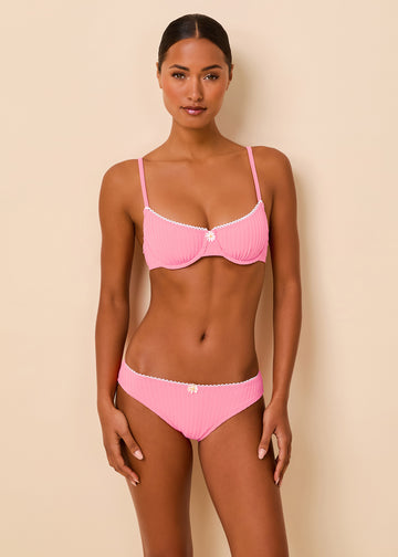 A woman modeling a pink ribbed two-piece bikini with white trim against a solid beige background.